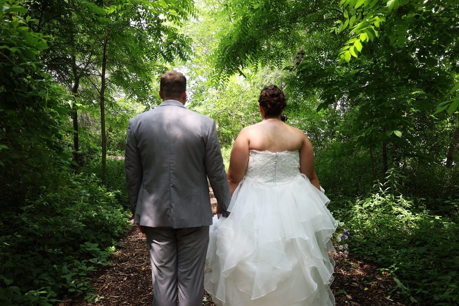 Bride and groom walking hand in hand down a green garden path