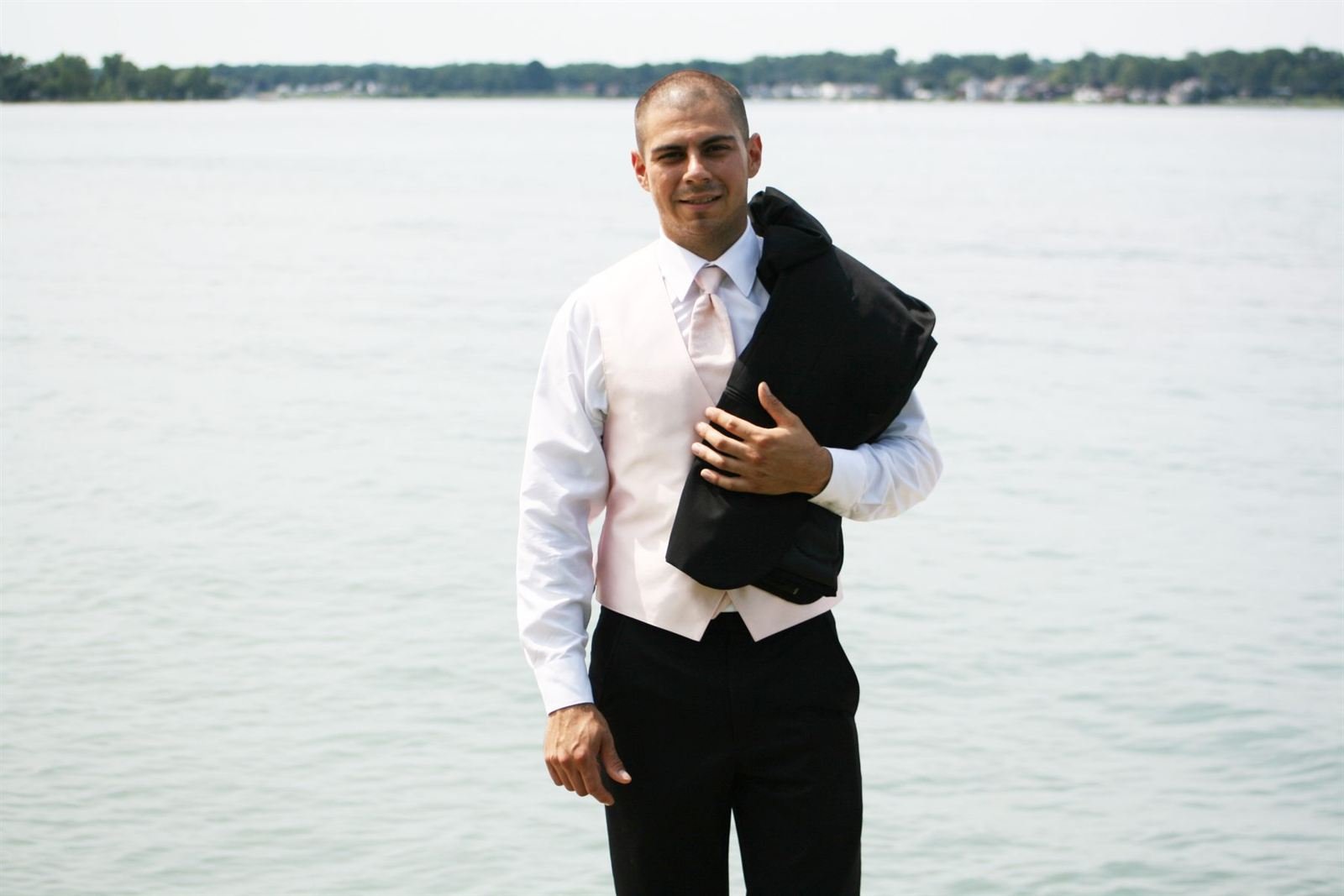 Groom by the water — groom holding his jacket by a lake